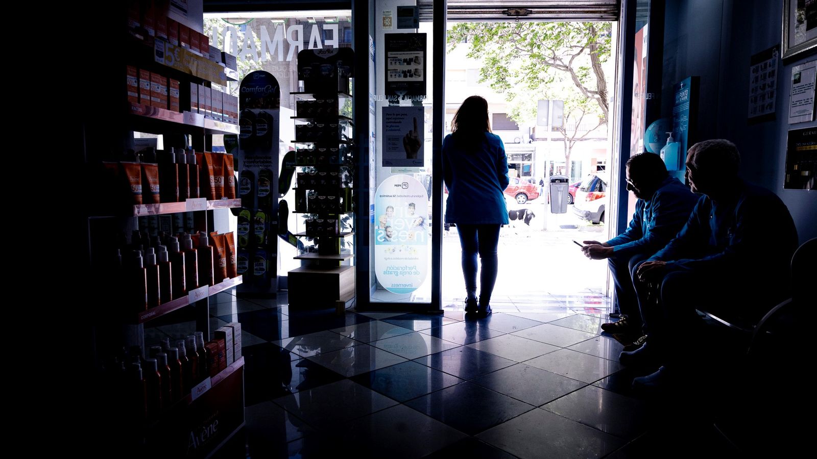 Clientes de una farmacia de Cádiz casi en penumbra aguardan en el interior del local el restablecimiento del suministro eléctrico.
