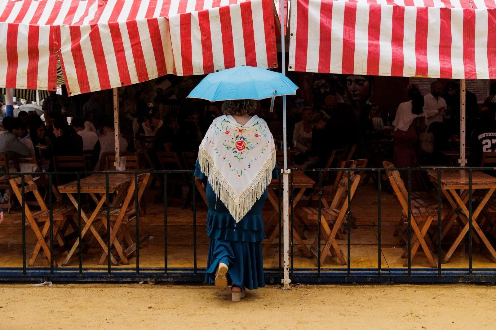 Una mujer vestida de gitana se protege con un paraguas a las puertas de una caseta.