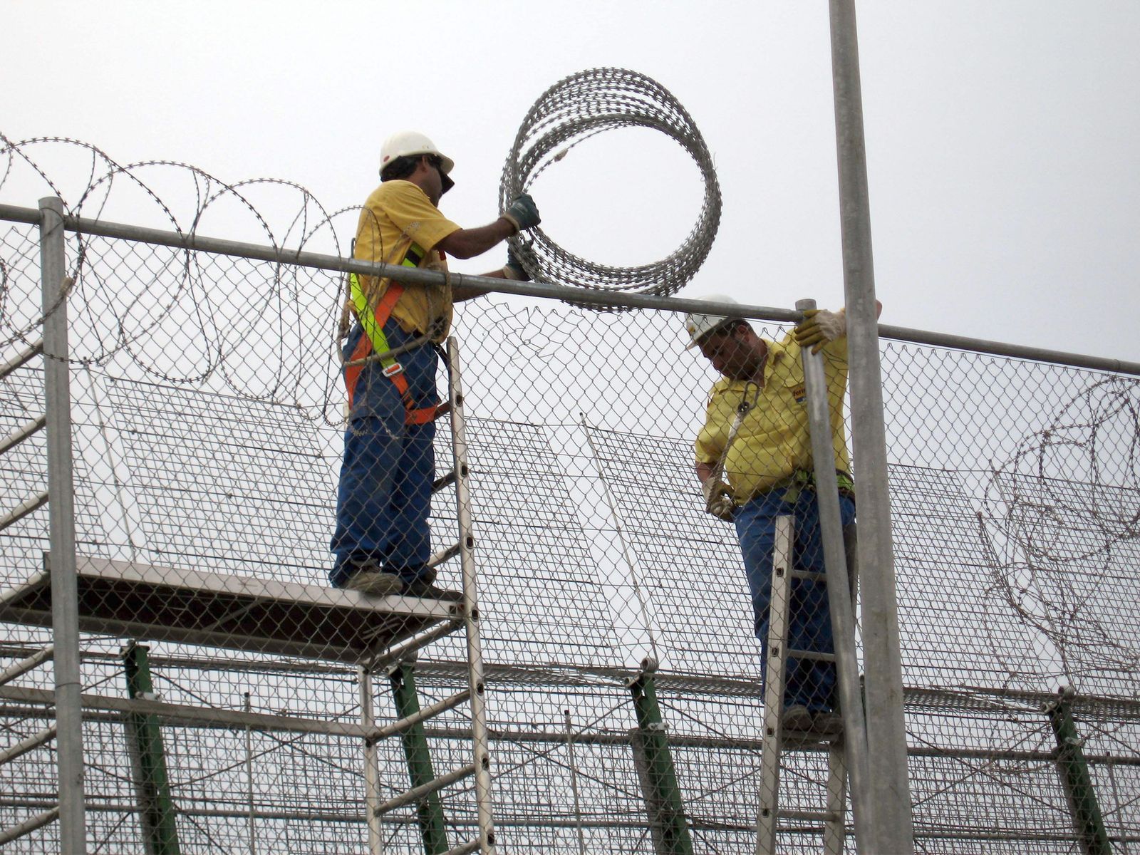 Dos operarios reparan las concertinas en la valla de Melilla, en la frontera entre España y Marruecos.