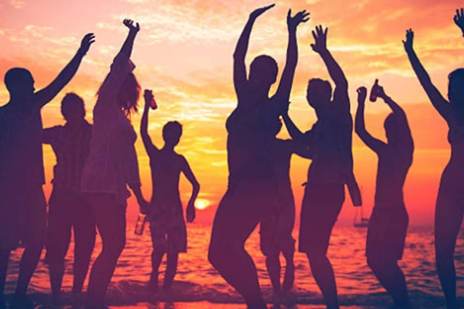 Un grupo de personas sigue el ritmo de la música junto al mar al atardecer.