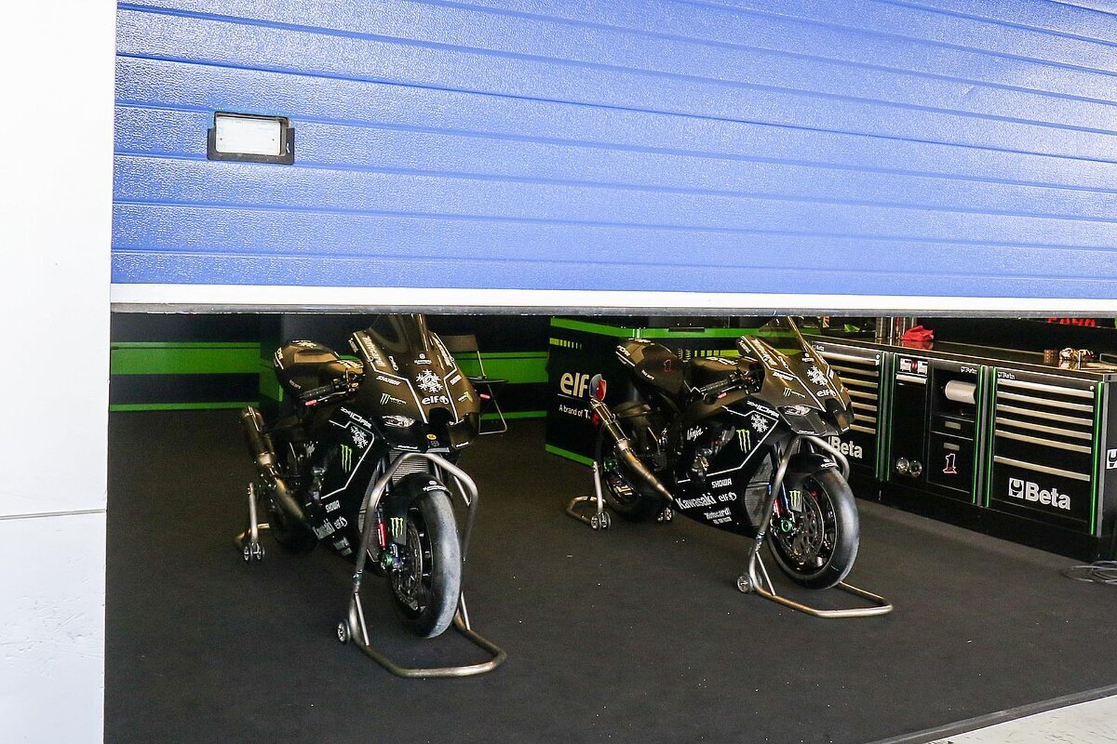 Las motos del Kawasaki Racing Team, en el box con la persiana medio bajada.