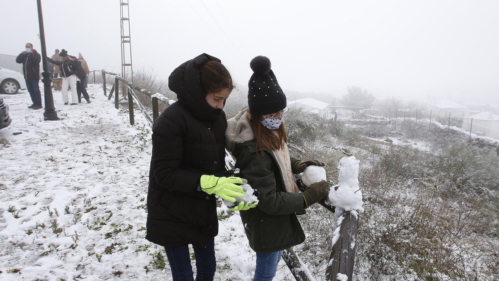 Dos niñas hacen un muñeco de nieve.