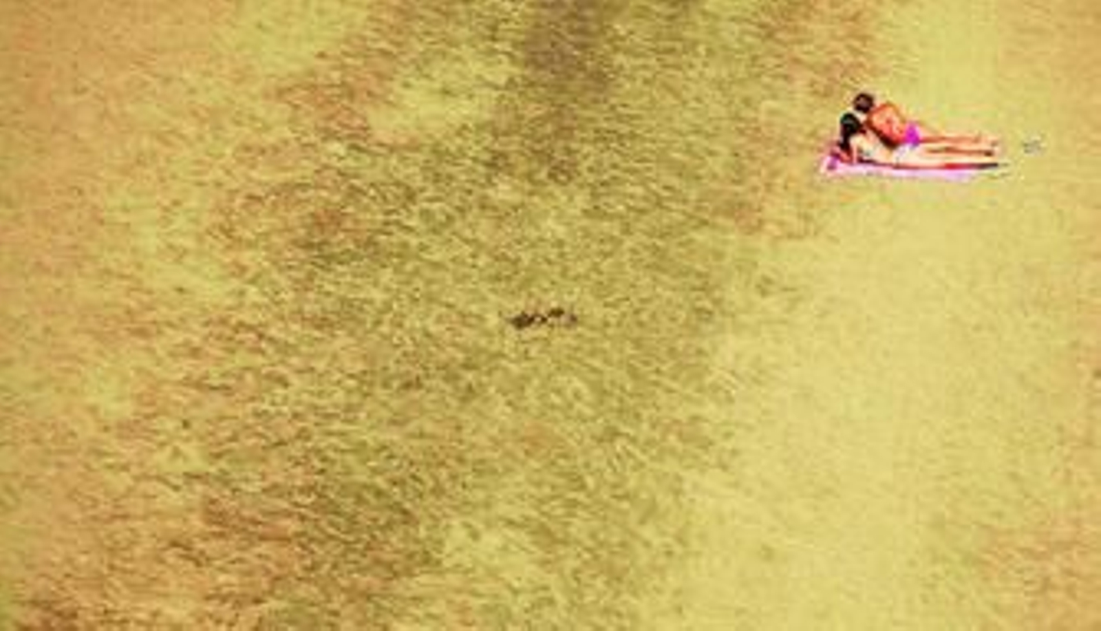Dos mujeres toman el sol en una zona solitaria de la playa de Rincón de la Victoria.