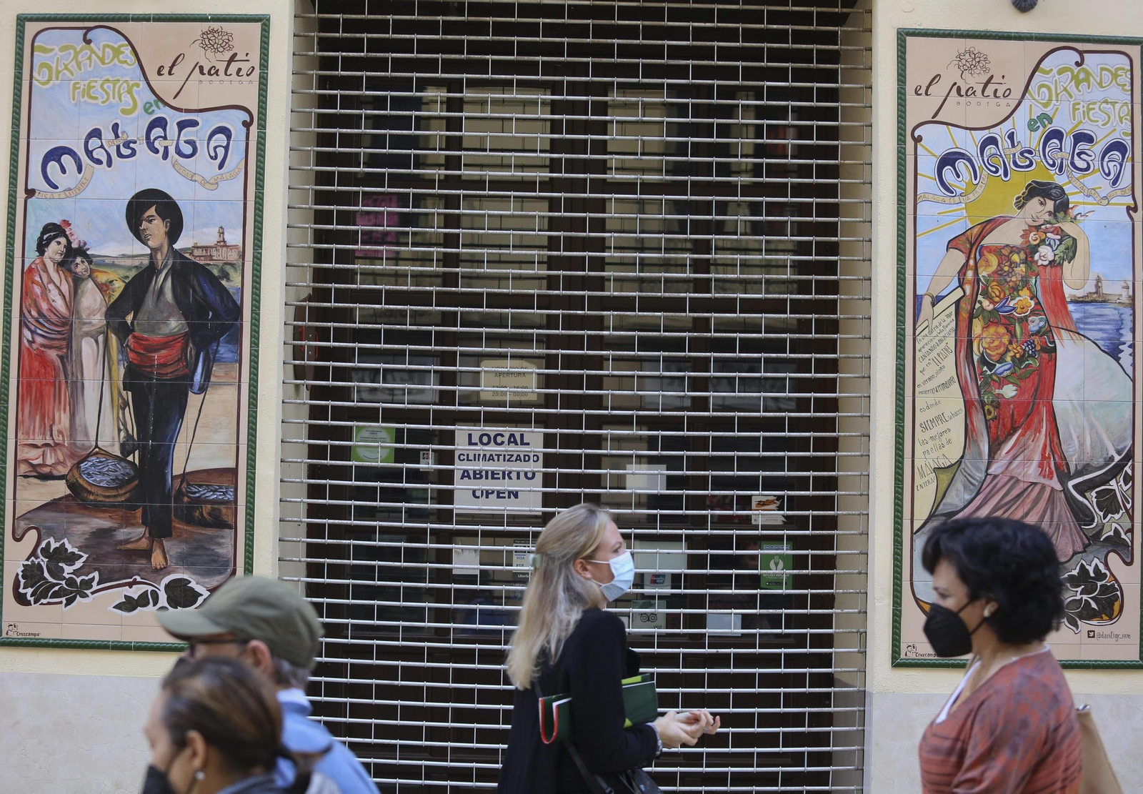 Varias personas pasan delante de un restaurante cerrado, en Málaga capital.