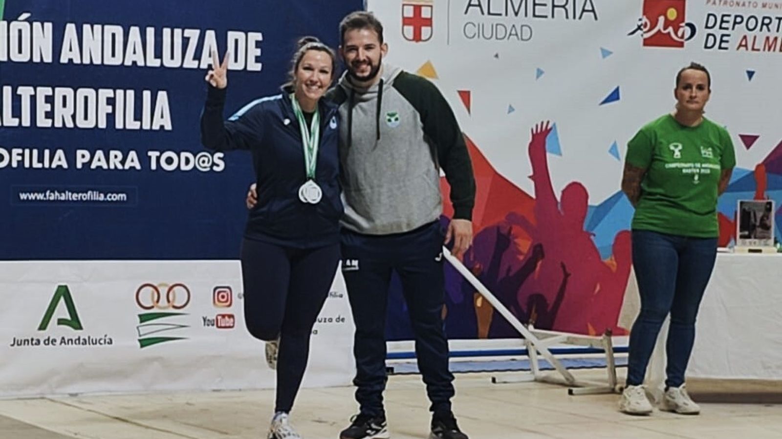 La haltera Evelyn Muñoz posa junto a su entrenador con sus medallas colgadas al cuello.