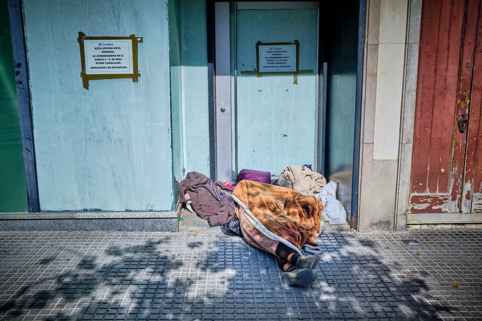 Una persona sin hogar, a las puertas de un local cerrado.
