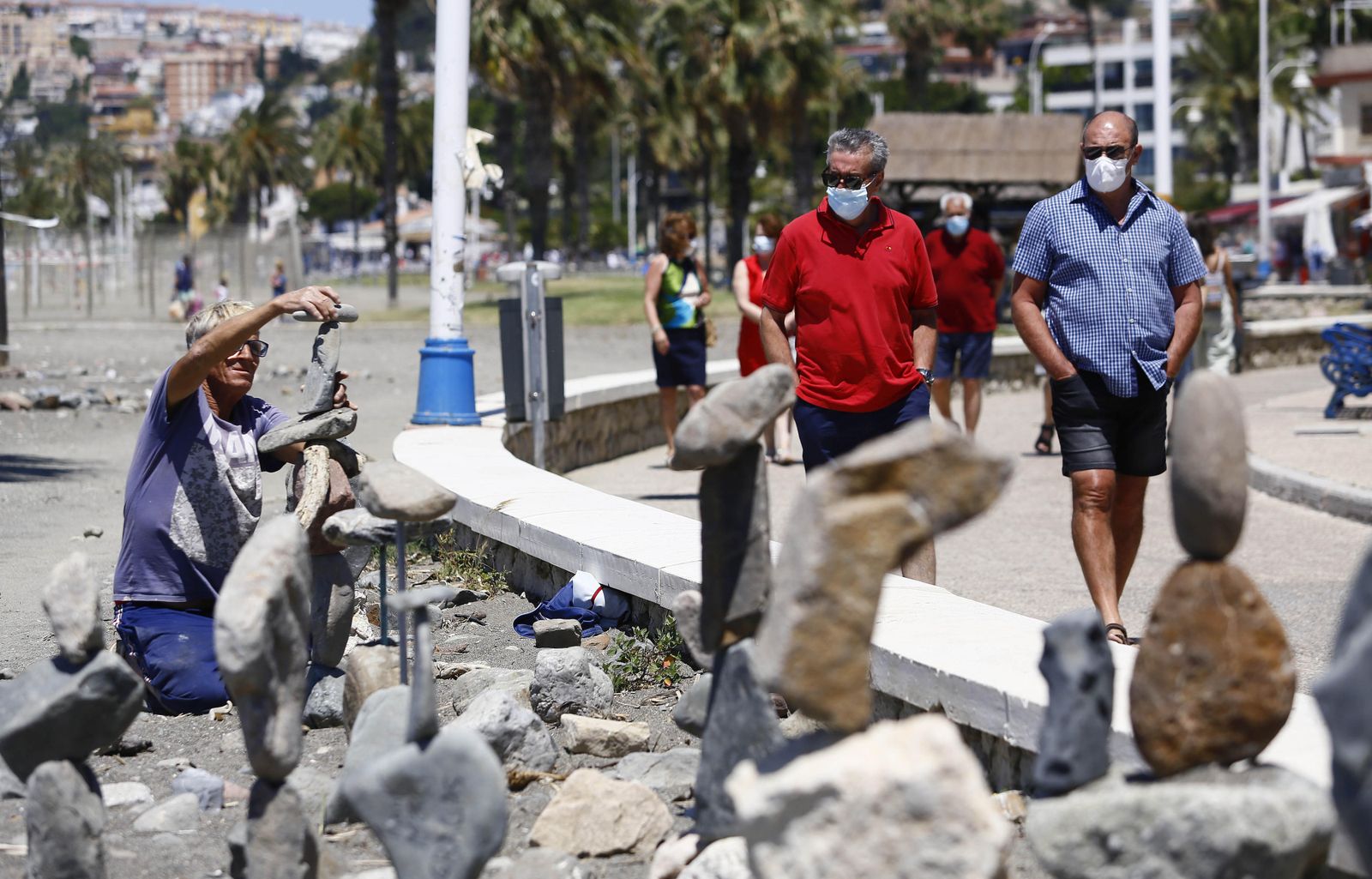 Dos hombres protegidos con mascarillas caminan por el paseo marítimo.