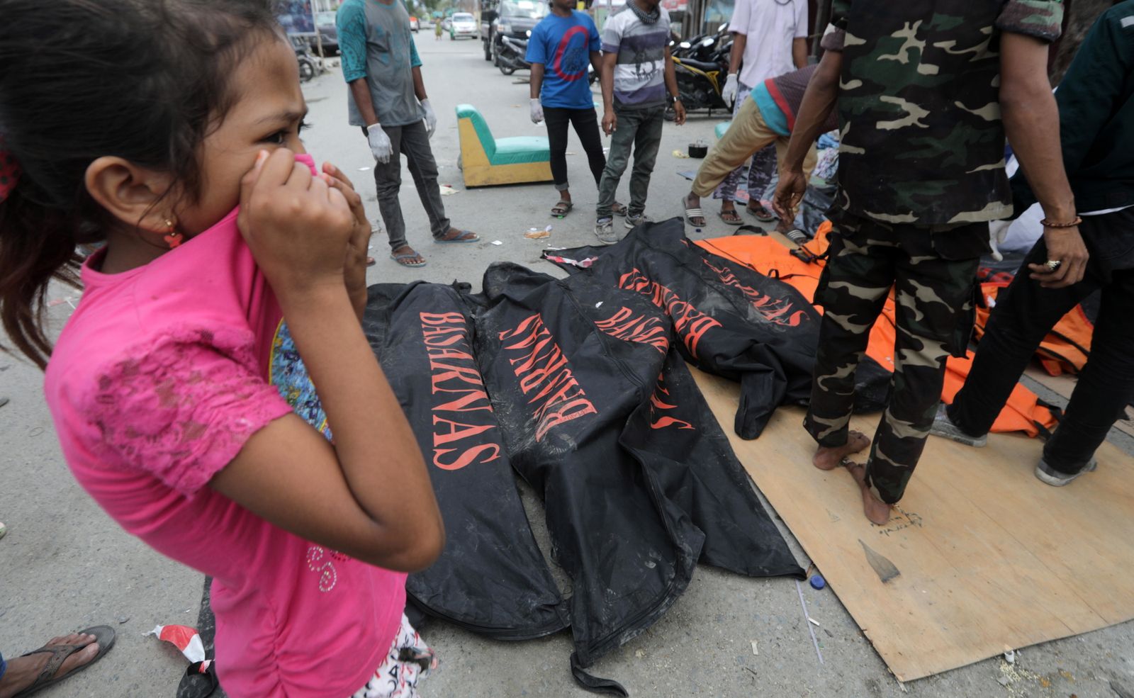 Una niña se tapa la nariz al pasar por delante de cuerpos recuperados.