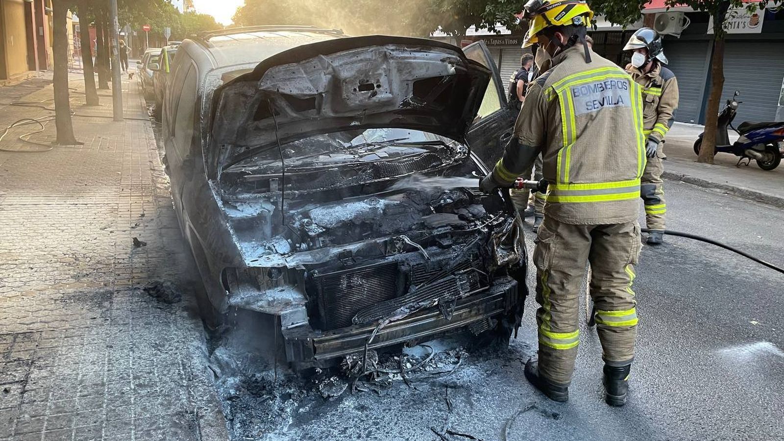 Los Bomberos apagan el incendio de uno de los coches quemados en la calle Venecia.