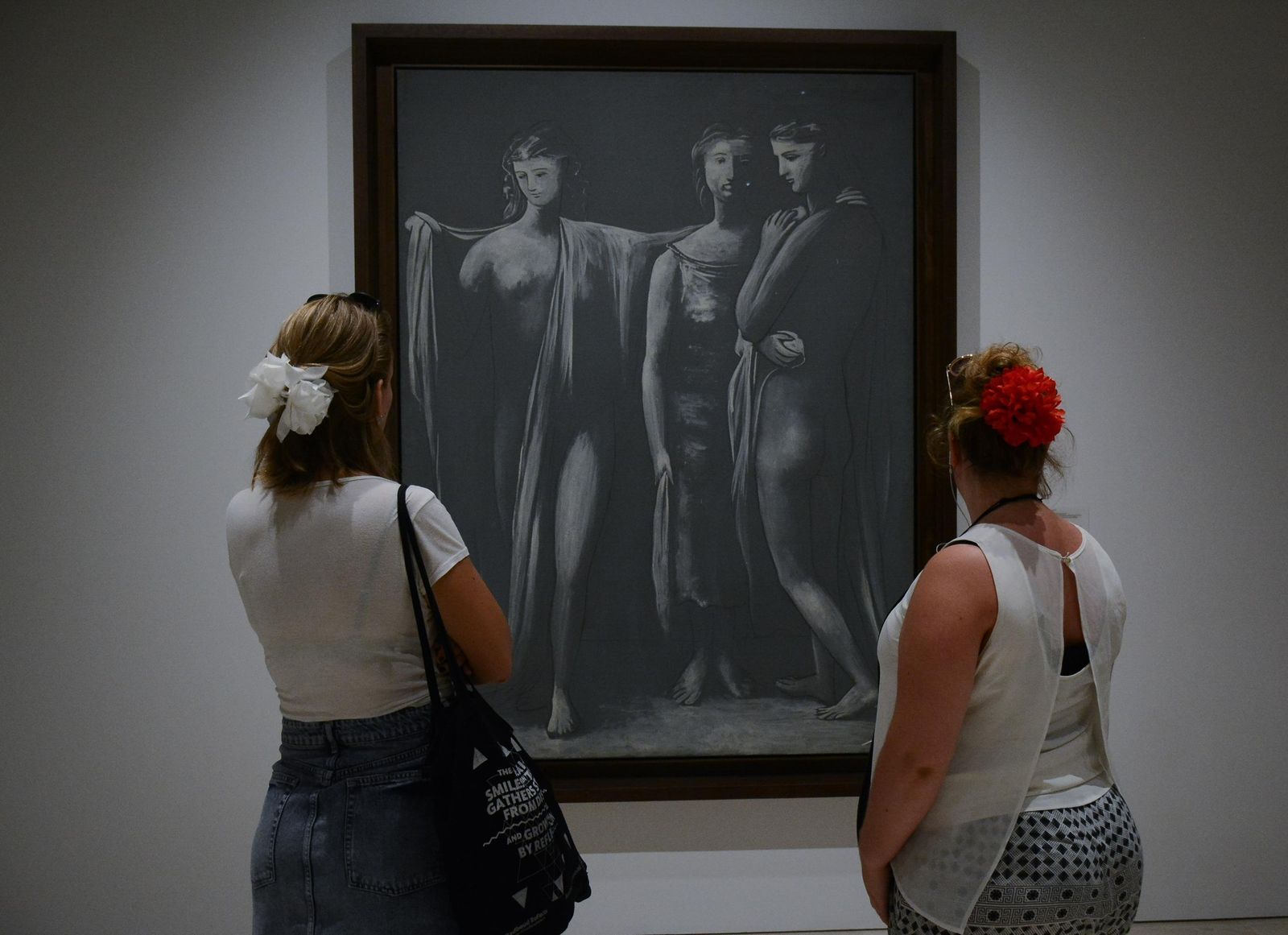 Dos mujeres con una flor de feria en el pelo observan un cuadro de la colección del Museo Picasso.