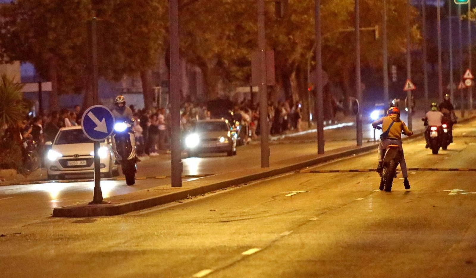 Un motorista hace un caballito tras una adelanto temerario a un turismo en presencia de público que celebra la maniobra.