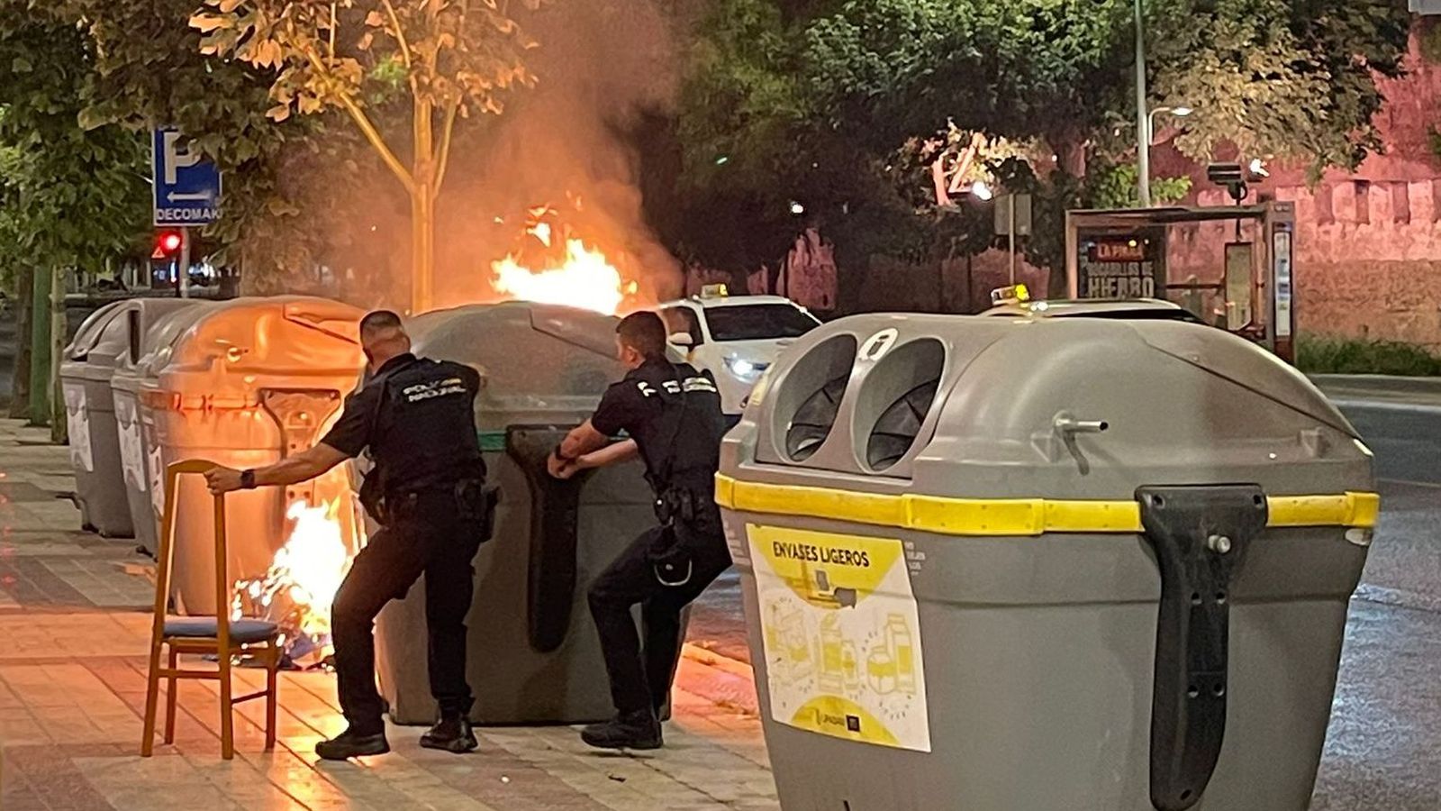 Dos policías nacionales separan un contenedor para evitar la propagación de las llamas.