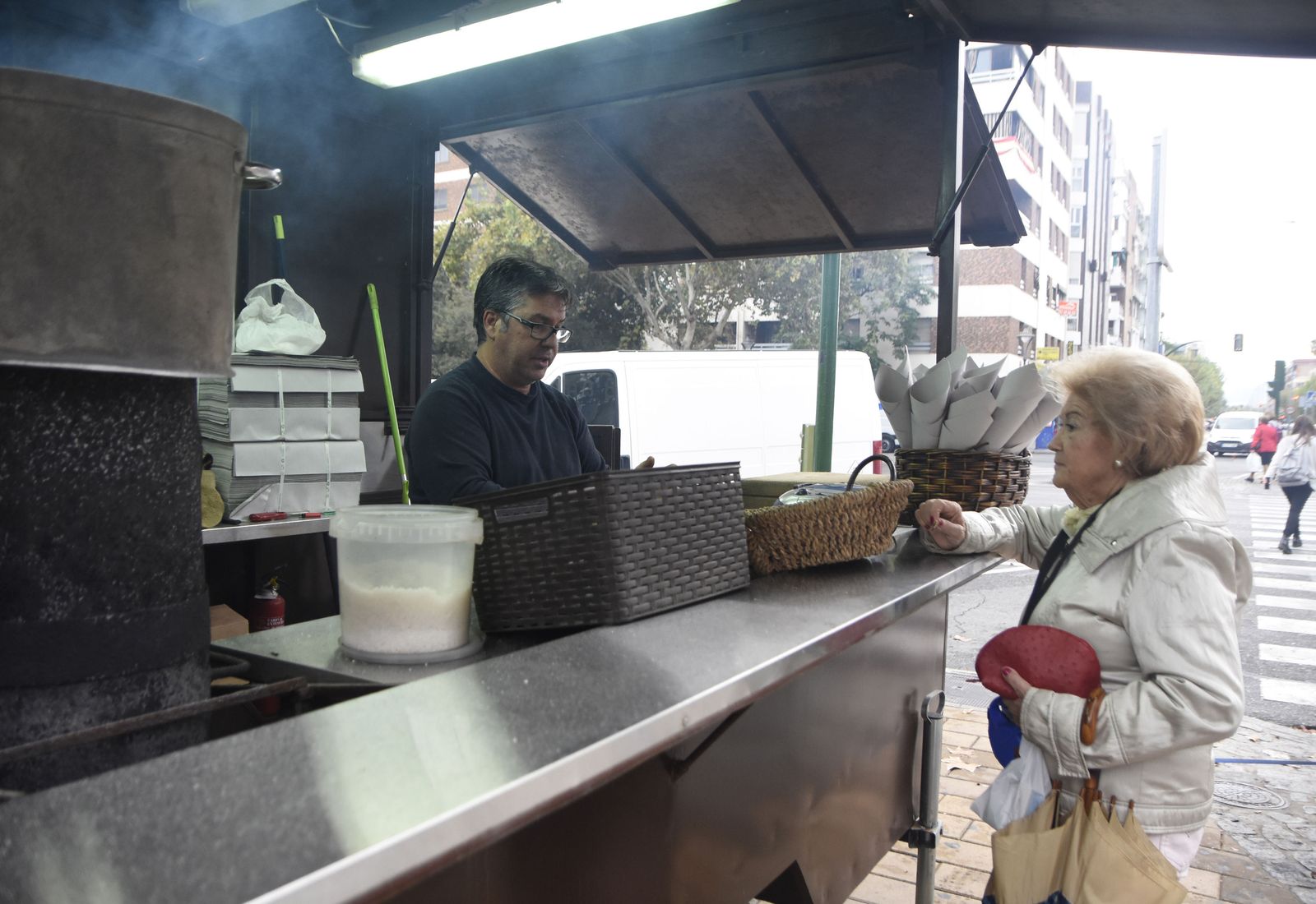 Un vendedor atiende a una clienta en un puesto de castañas.