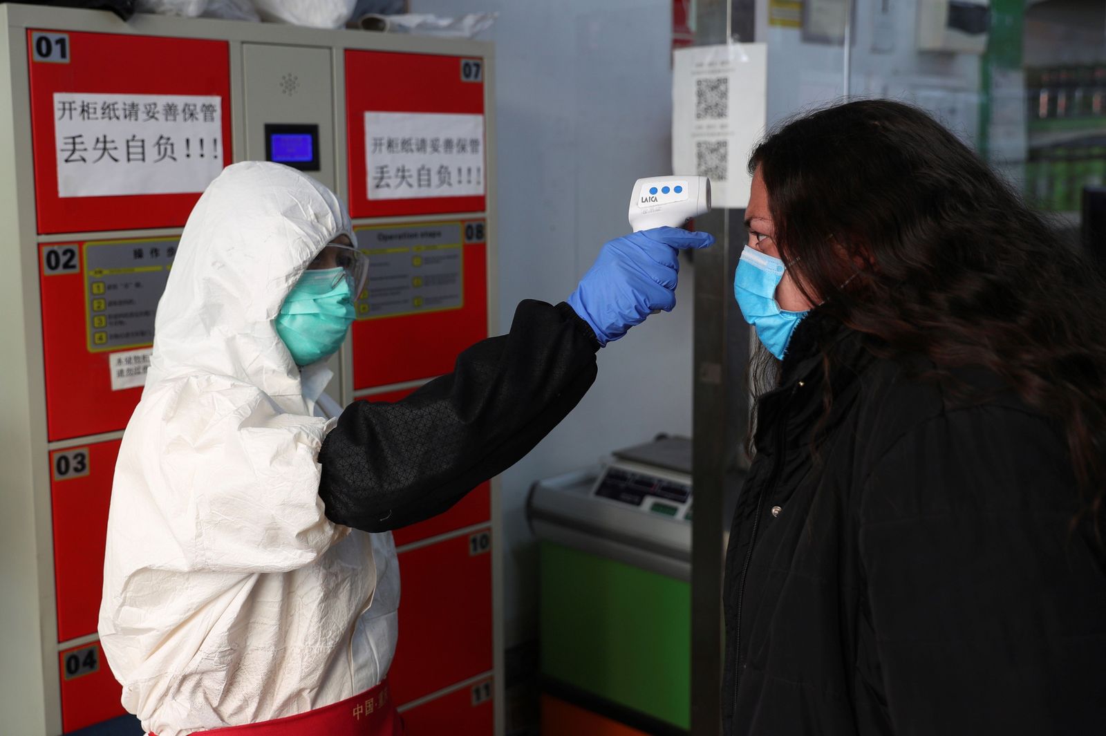 Una trabajadora usa un termómetro  de infrarrojos  para tomar la temperatura a los clientes durante la reapertura del supermercado.