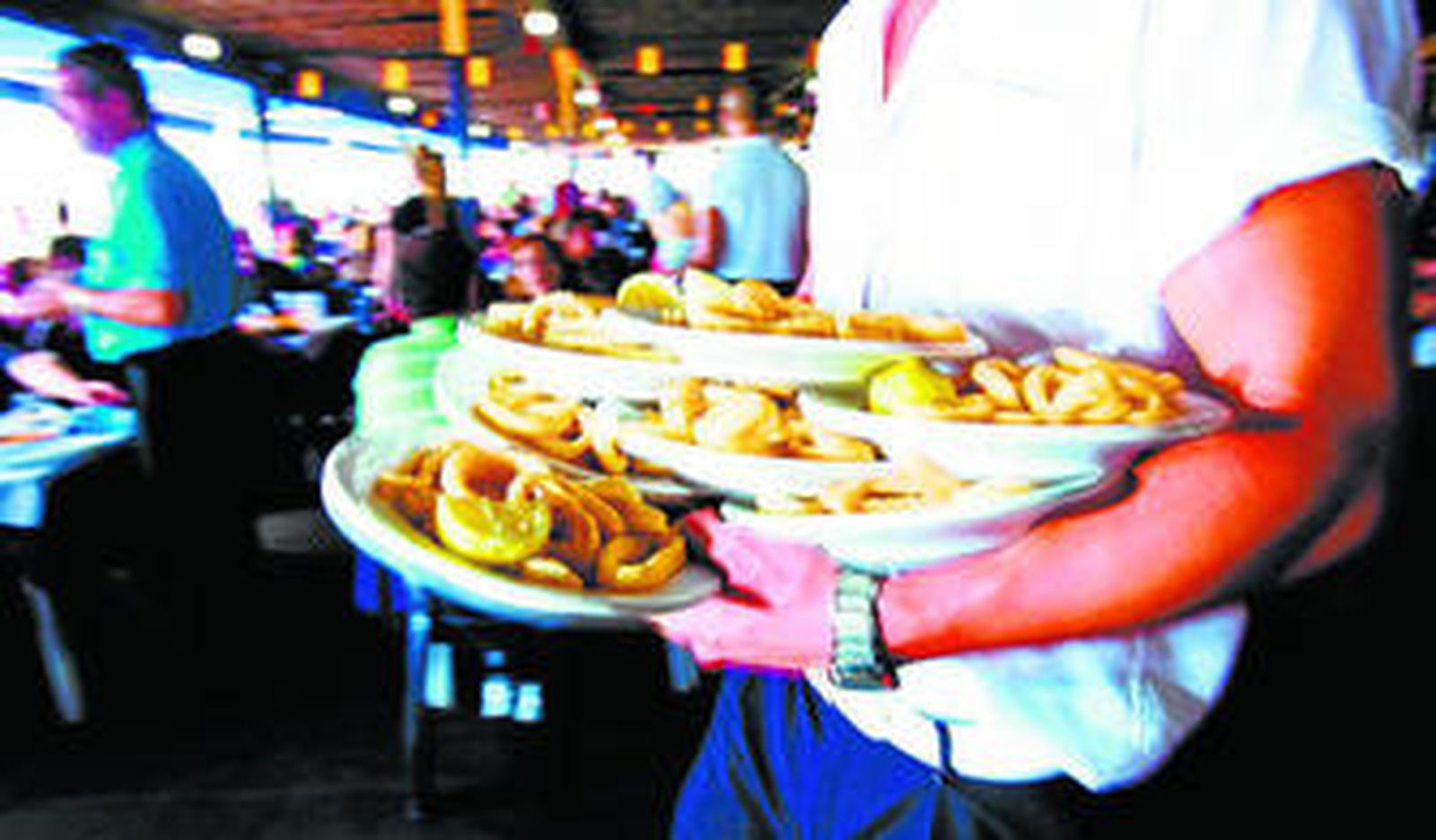 Un camarero porta varios platos en un chiringuito.