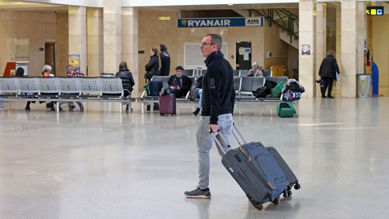 Pasajeros en el aeropuerto de Jerez con una publicidad de Ryanair al fondo