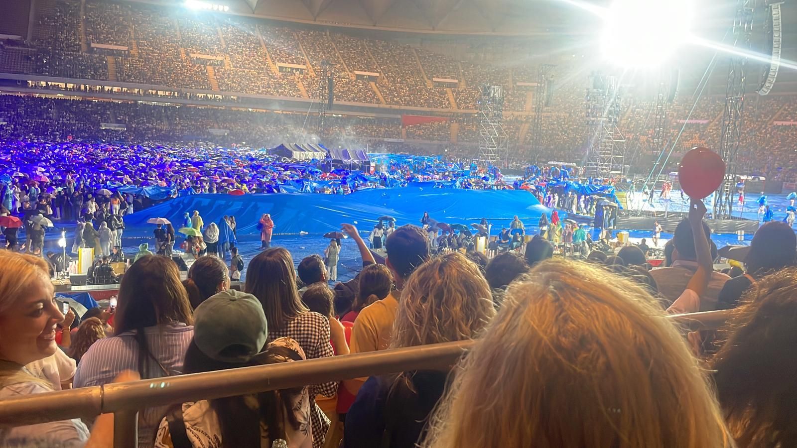 Varios asistentes se cubren con la lona del césped del Estadio de La Cartuja.