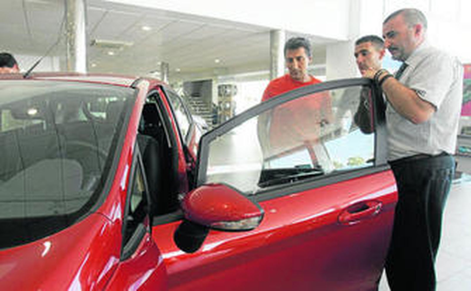 Un vendedor de coches enseña un vehículo a dos posibles compradores.