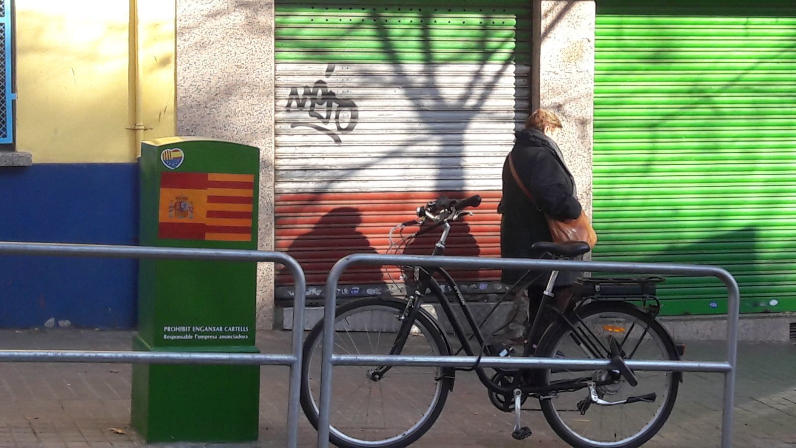 Una mujer pasa delante de un buzón con una pintada de la bandera Española y de Cataluña