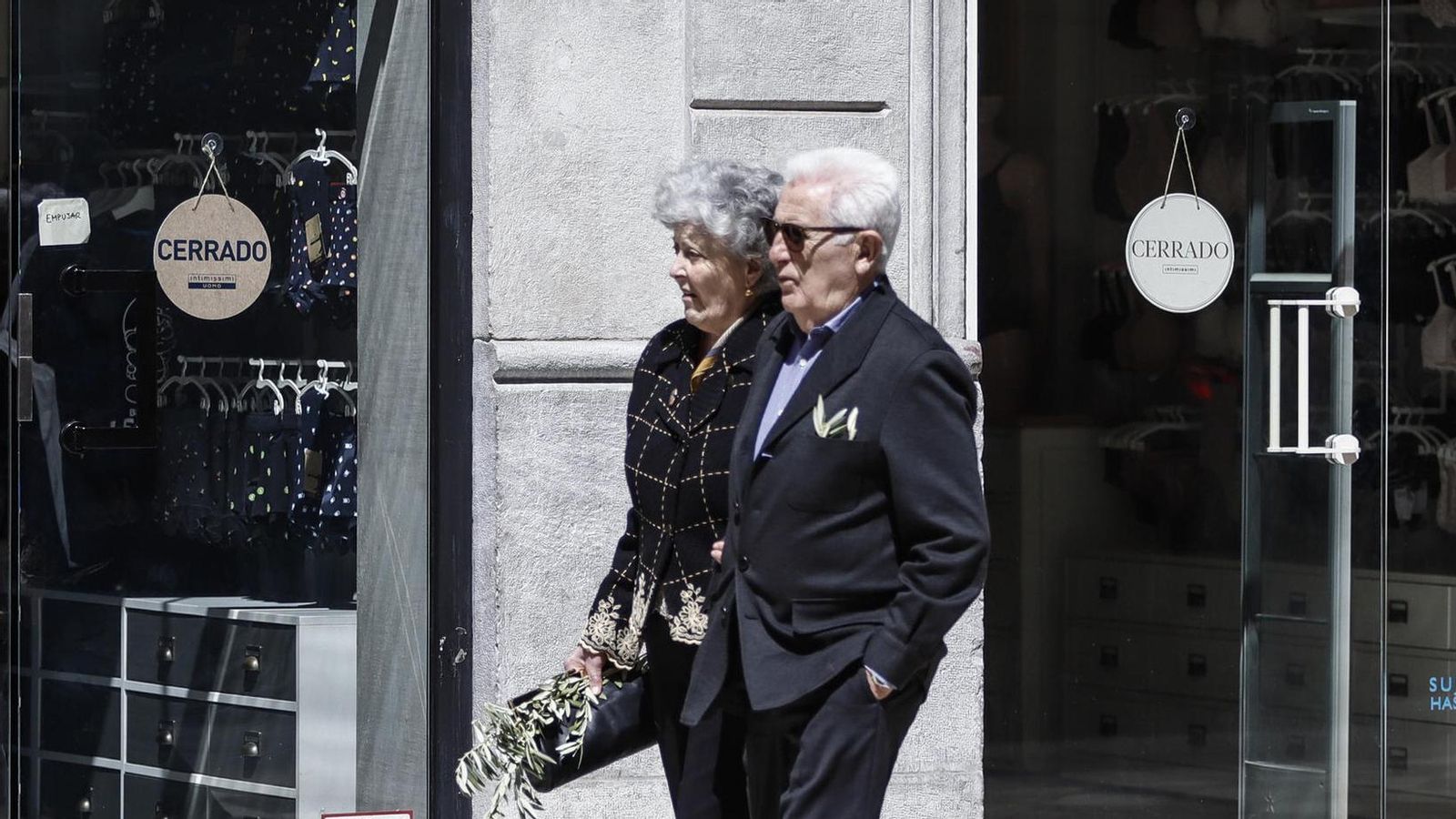 Una pareja camina por el centro de Granada frente a una tienda cerrada
