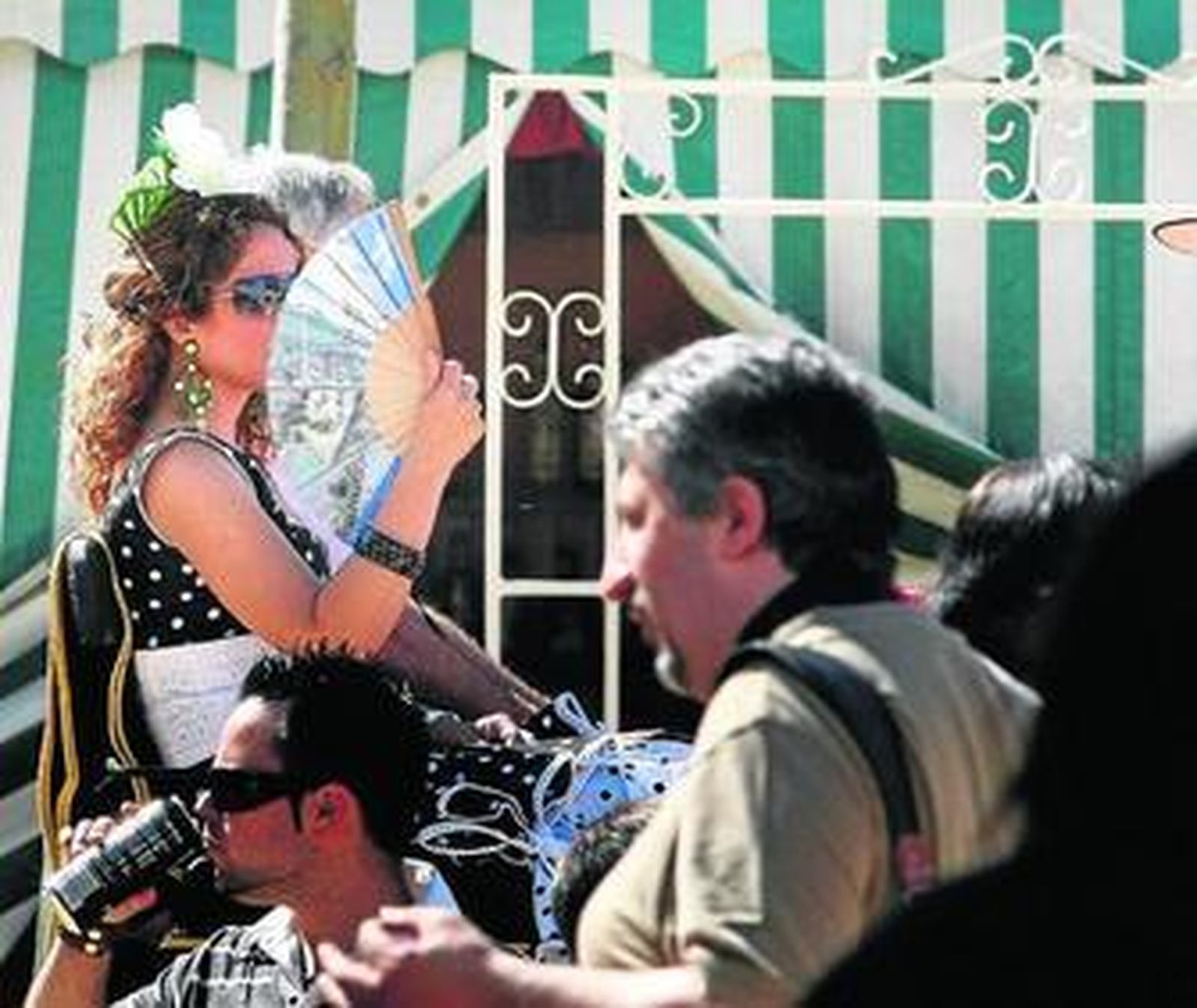 Una joven vestida de flamenca se abanica mientras pasea en un coche de caballos.