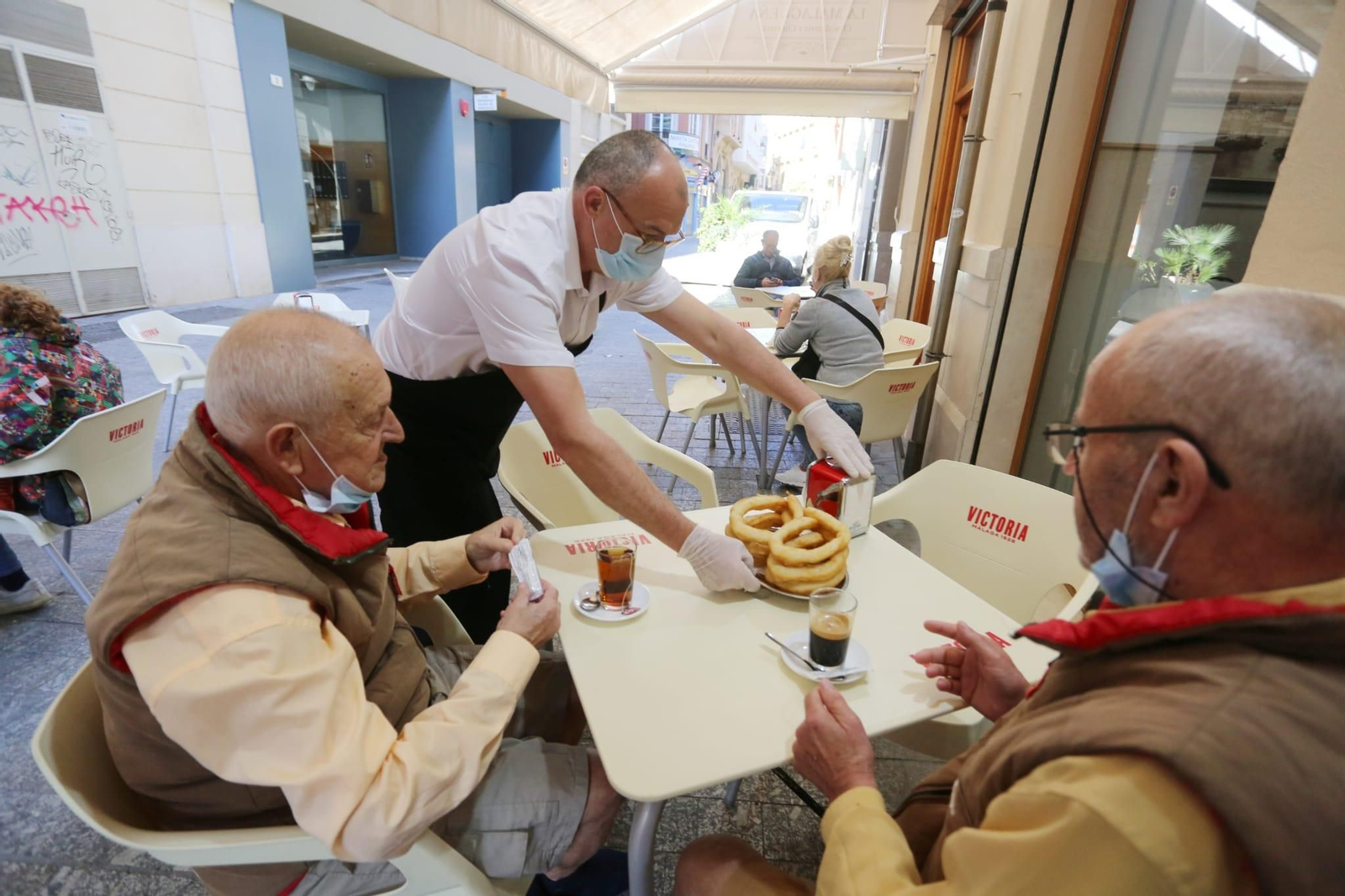 Un camarero sirve café con churros a dos clientes en un bar del Centro.