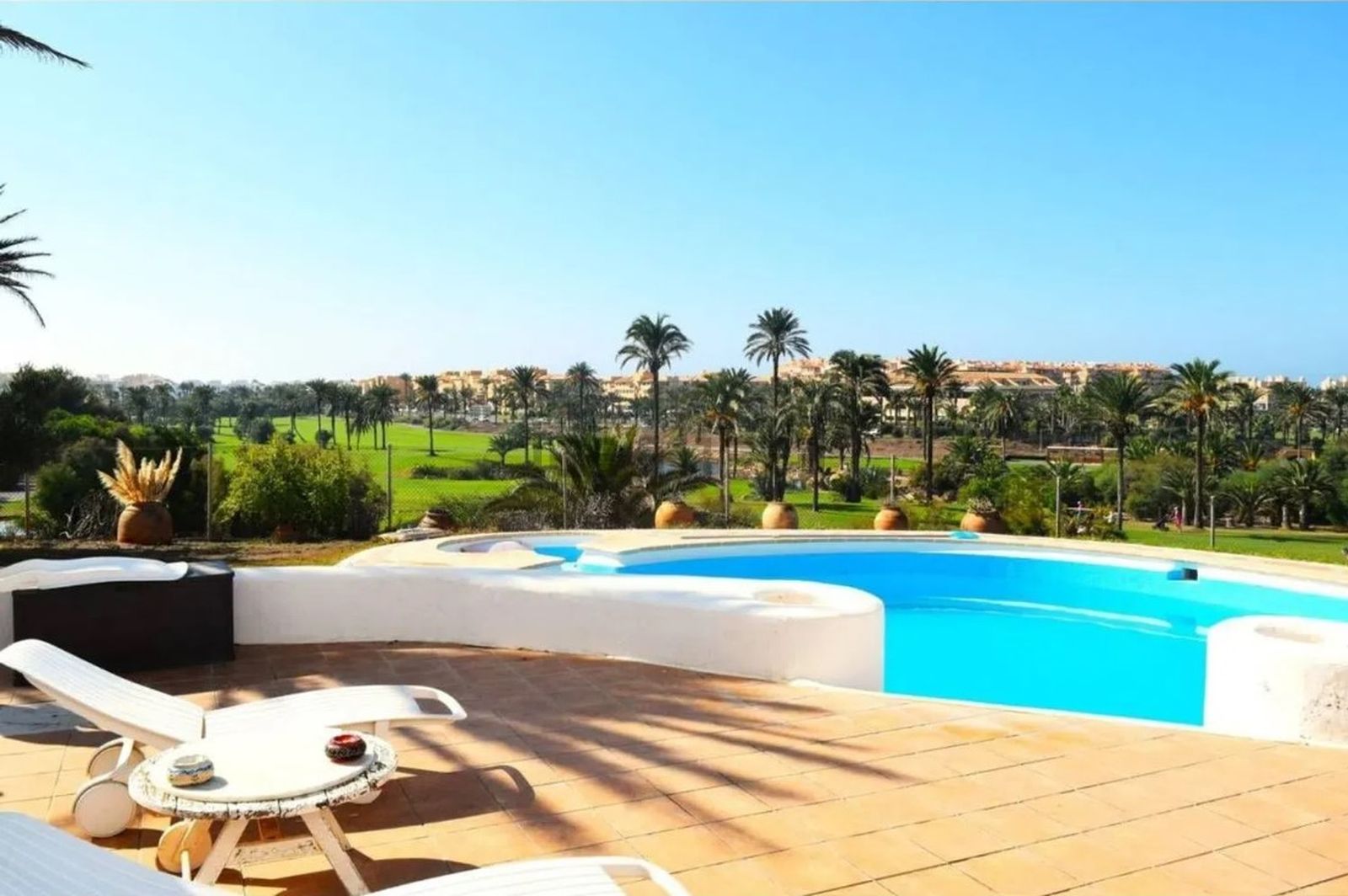 Zona exterior orientada al sur, con piscina en primer plano y vistas abiertas al golf, al puerto deportivo y a la línea de costa.