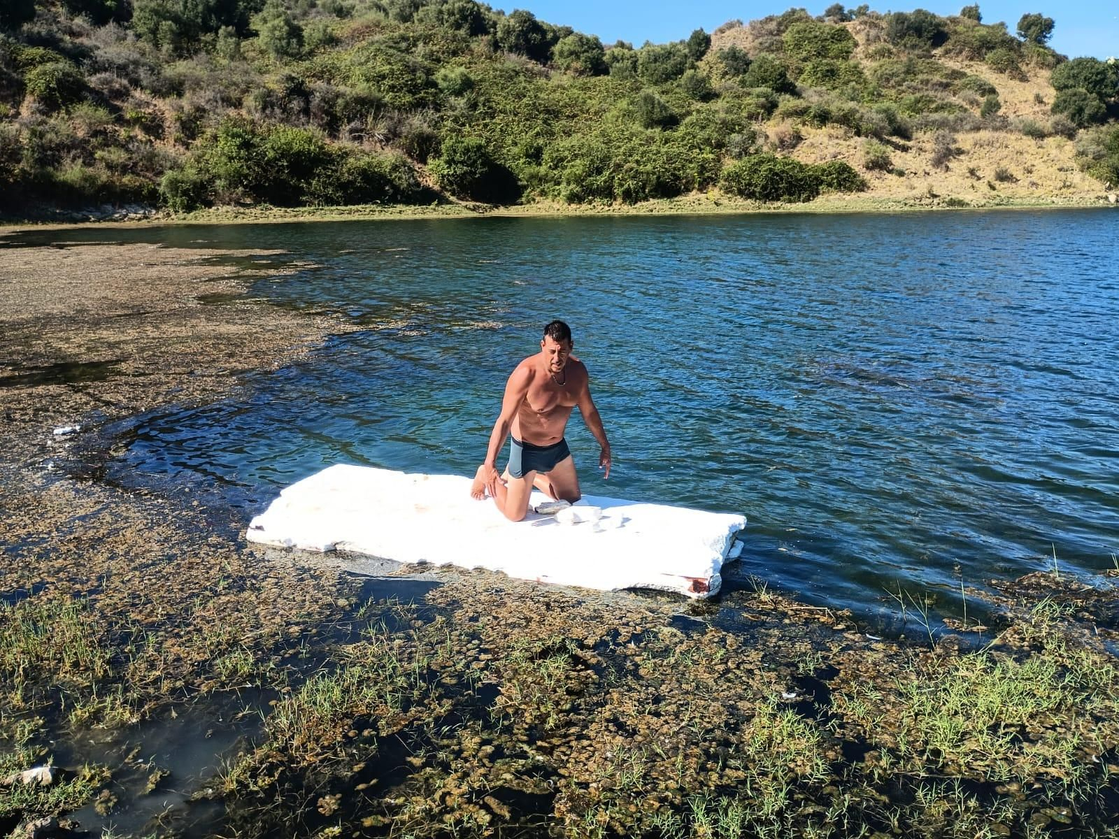 El voluntario Tony Moyano recoge los trozos más pequeños de corcho blanco 'navegando' por la laguna sobre la gran plancha.
