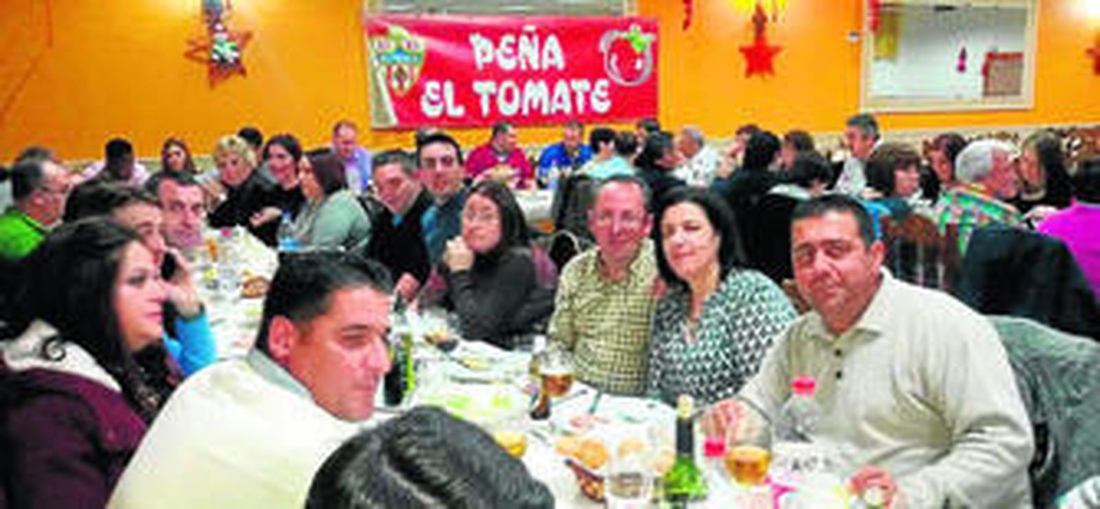 Peñistas brindando por la Navidad con la bandera del Tomate al fondo.