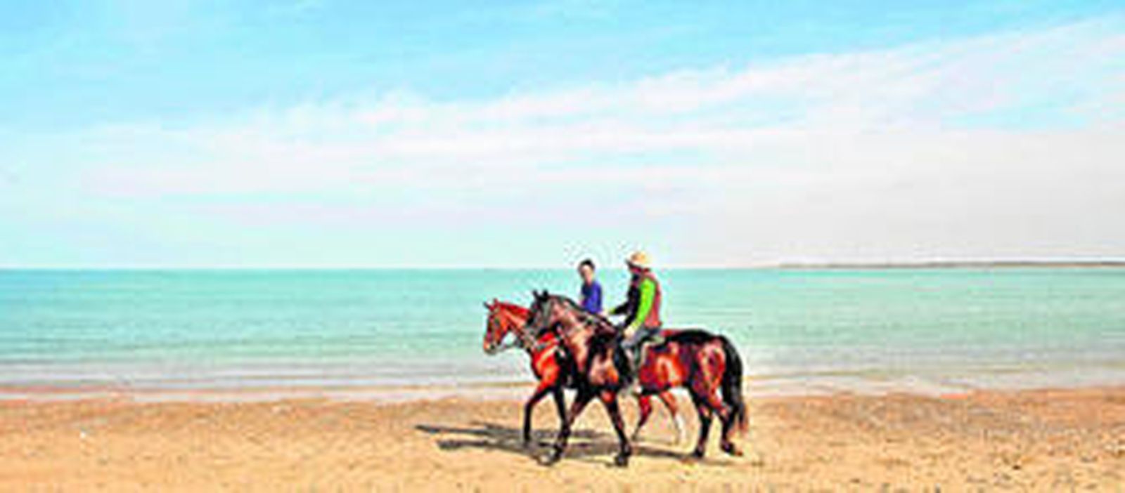 Dos jinetes con sus caballos paseando por la sanluqueña playa de Las Piletas.