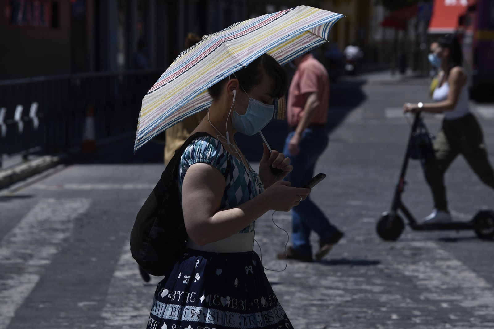 Una joven con mascarillas se protege del sol mientras maneja el móvil.