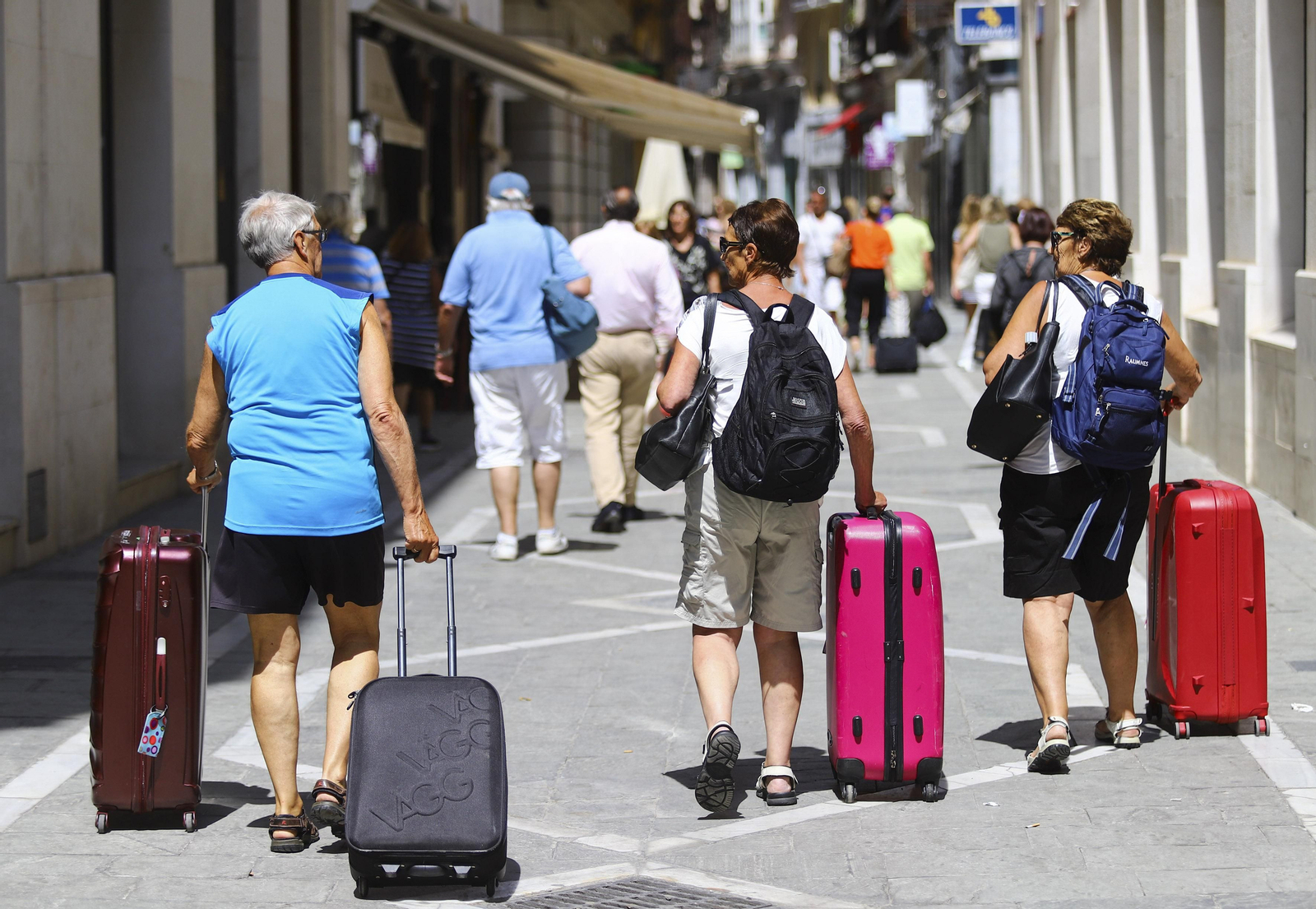 Un grupo de turistas pasea con sus maletas por una calle de Málaga.