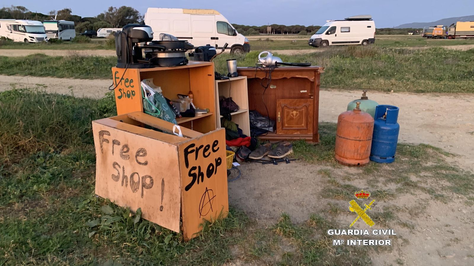 Un punto con varios muebles y enseres junto a varias furgonetas y autocaravanas en el campamento.