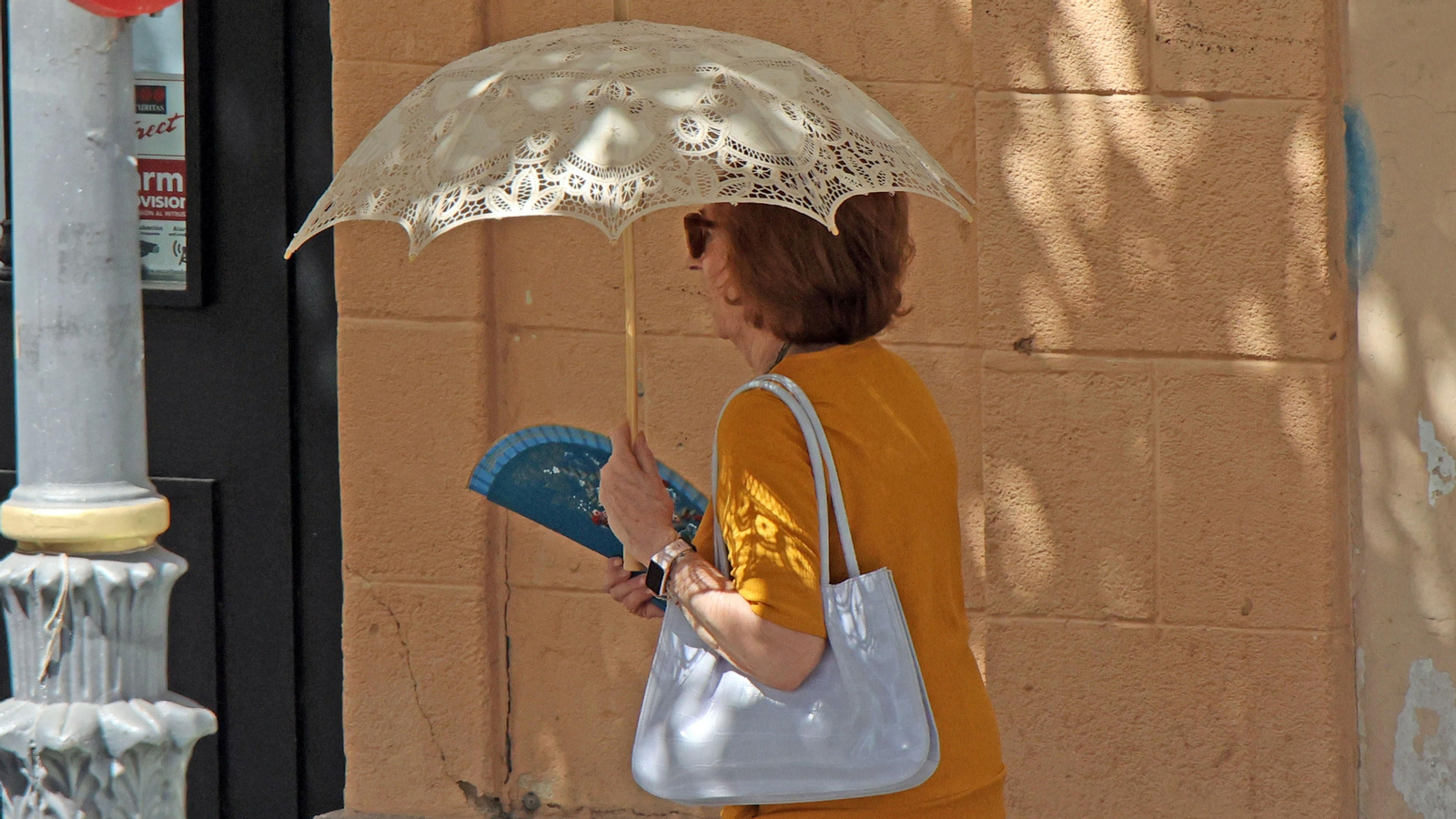 Una mujer con abanico y bajo una sombrilla, protegiéndose del sol.