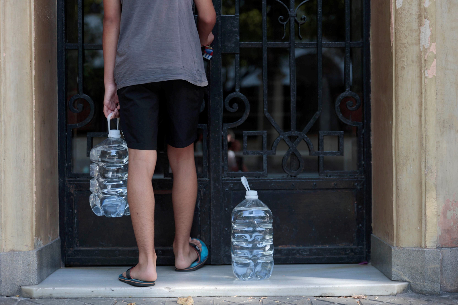 Un hombre abre un portal con dos garrafas de agua.