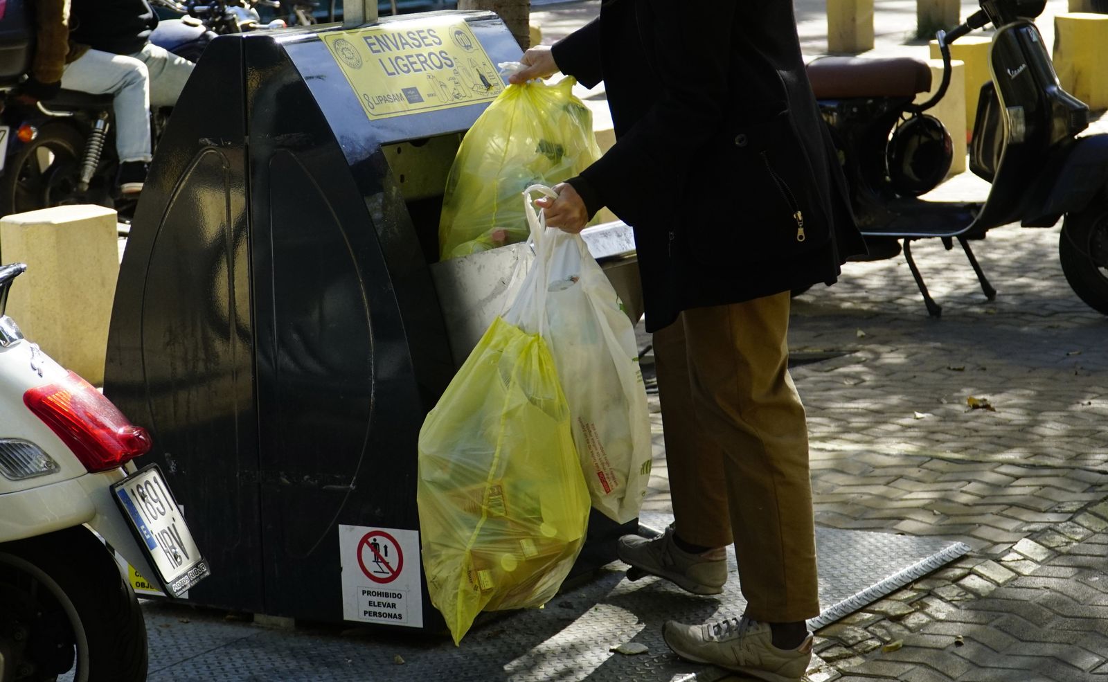 Un ciudadano introduce envases en un contenedor amarillo soterrado.