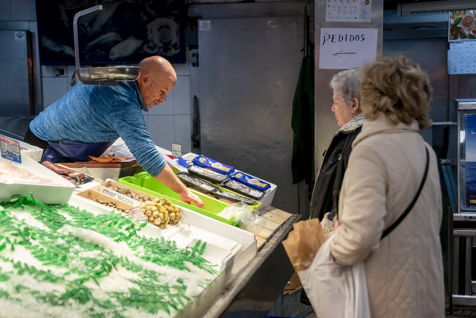 Un trabajador autónomo atendiendo a dos clientas en su pescadería.