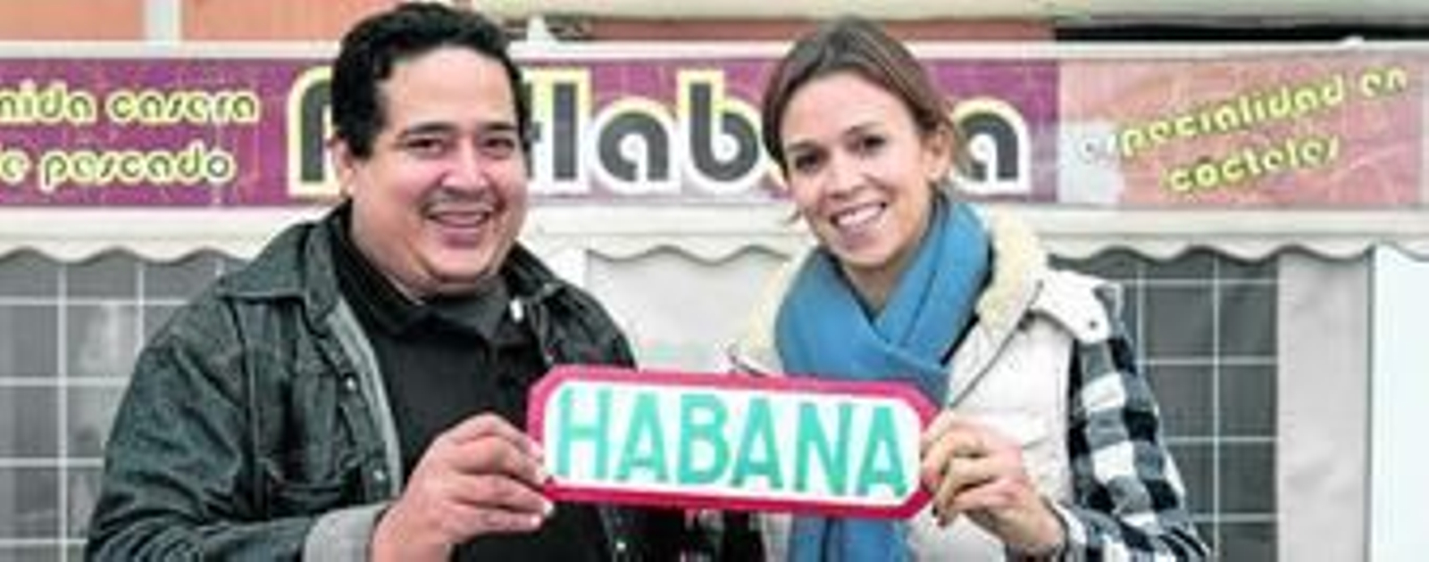 El cubano Ulises Tejeda y la estadounidense Anna Frandsen muestran un cartel alusivo a la capital caribeña ante el bar que regenta el primero en el Paseo Marítimo.