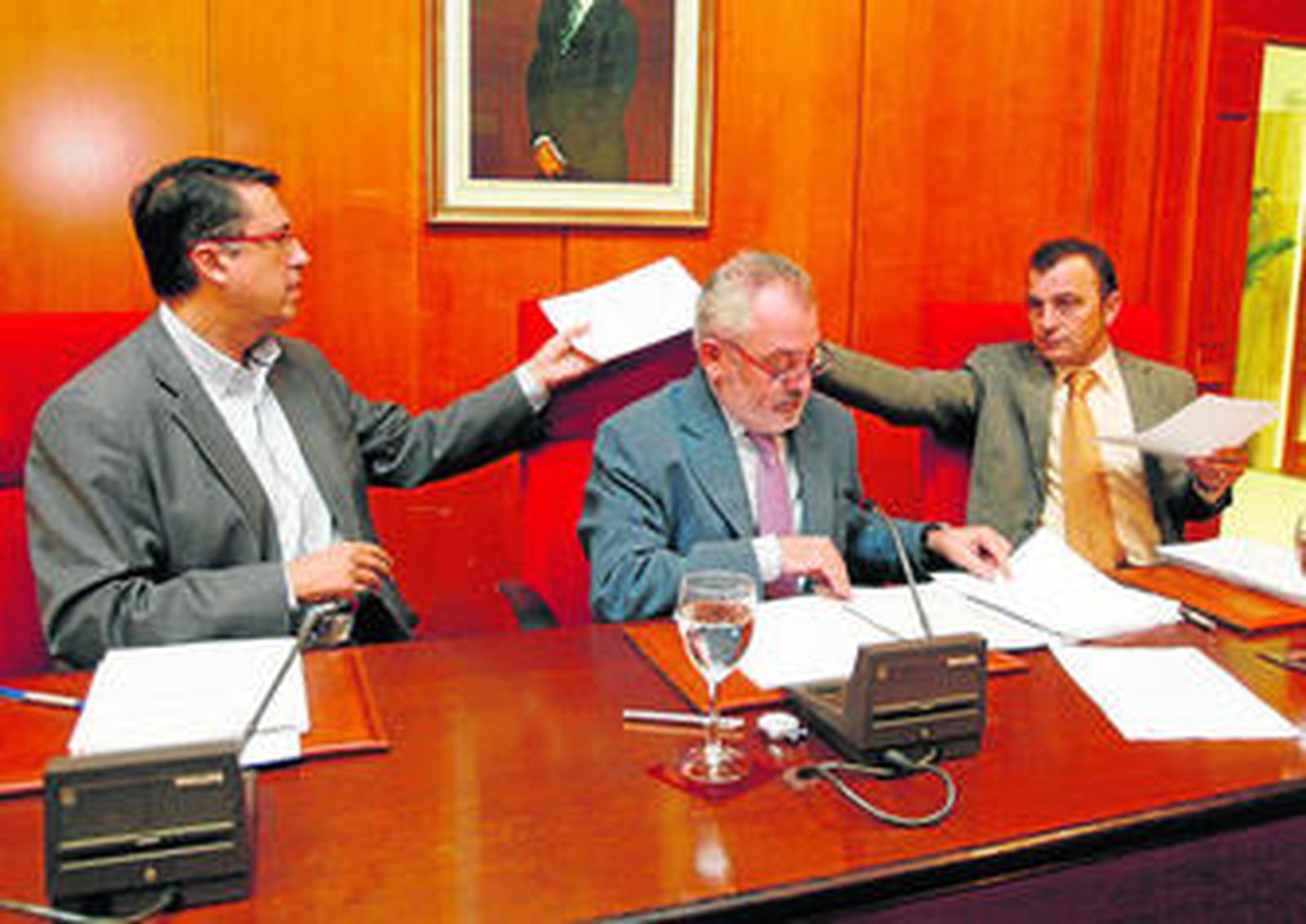 Rafael Blanco y Francisco Tejada intercambian documentos tras el asiento del alcalde en el salón de Plenos.