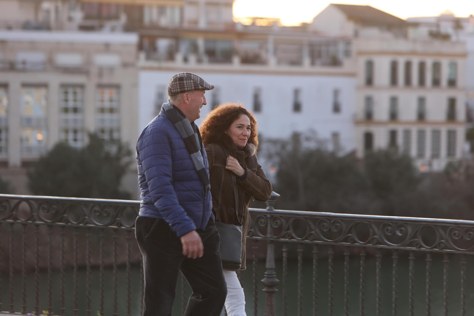 Dos personas pasean abrigadas por el puente de Triana.