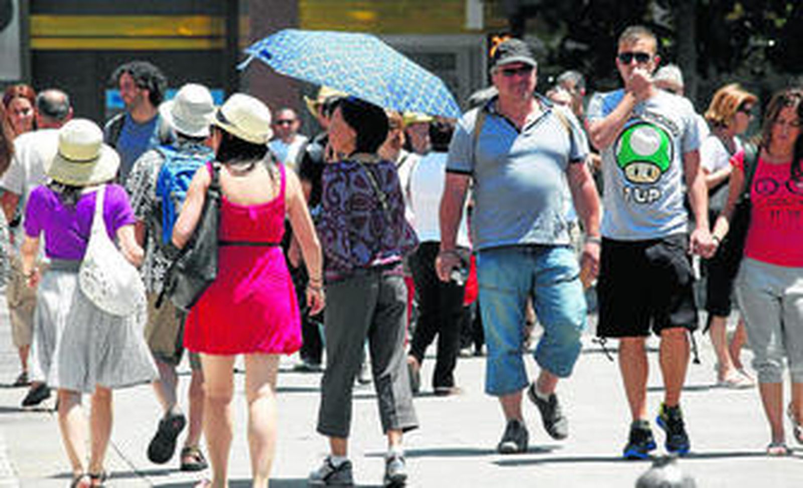 Los turistas pasean protegidos del sol y continúan dándole utilidad al paraguas hasta en el verano.