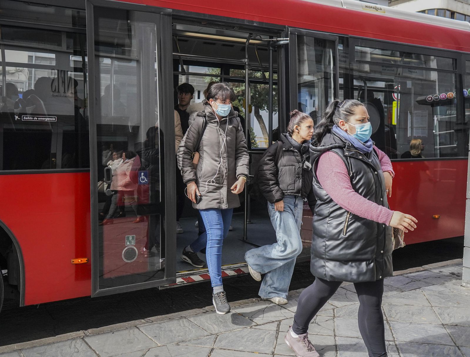 Varias personas, algunas con mascarilla y otras sin ella, bajan de un autobús en Granada.