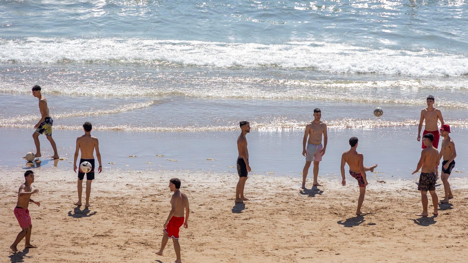Grupos de jóvenes juegan al balón en la orilla de Santa María del Mar.