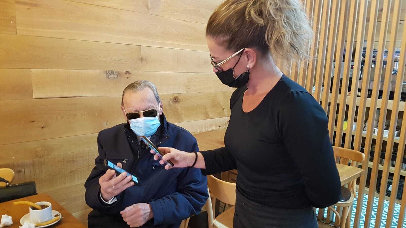 Una camarera procediendo a la lectura del certificado de uno de los clientes de una cafetería del centro.