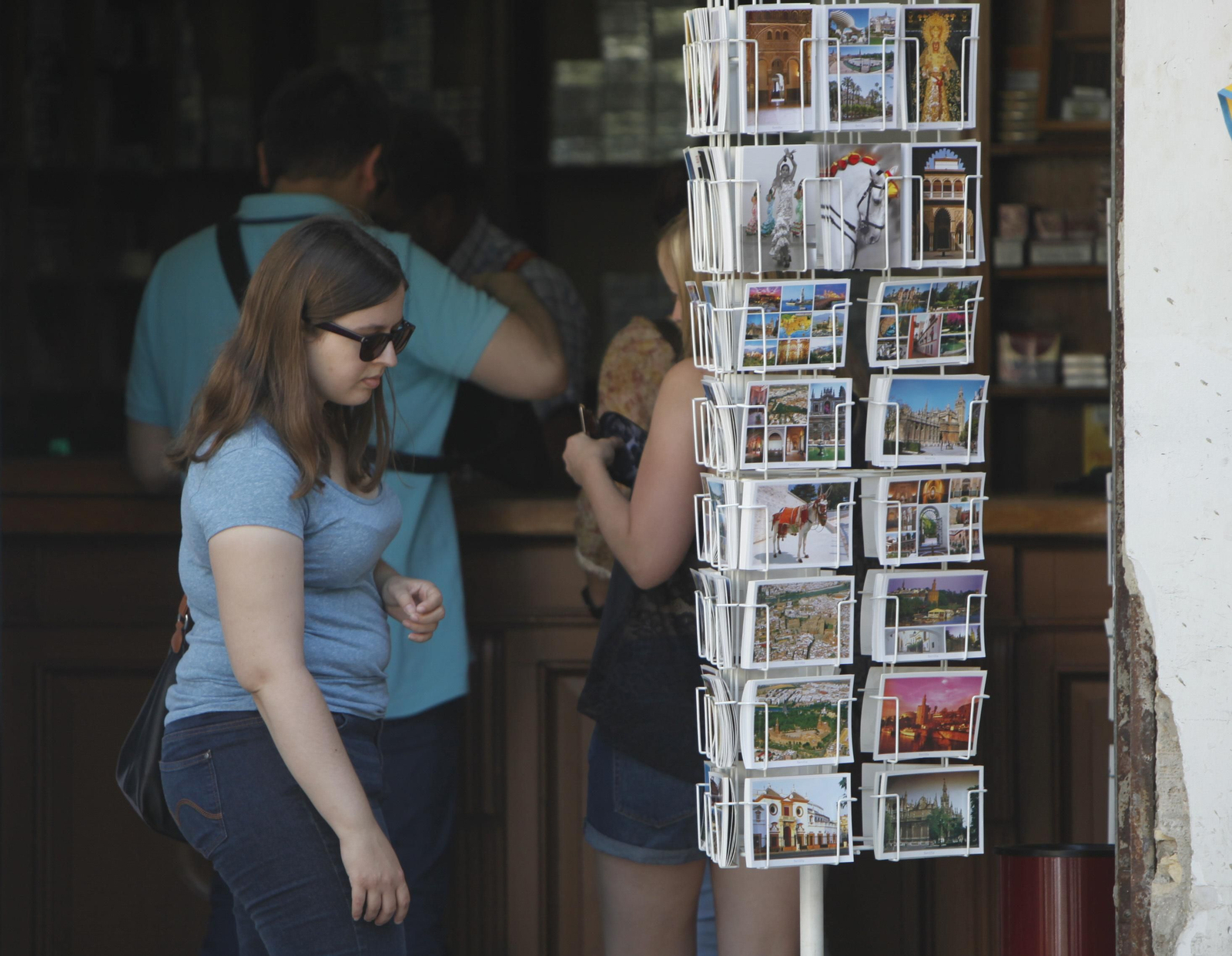 Una joven mira un estante con postales de la capital hispalense.