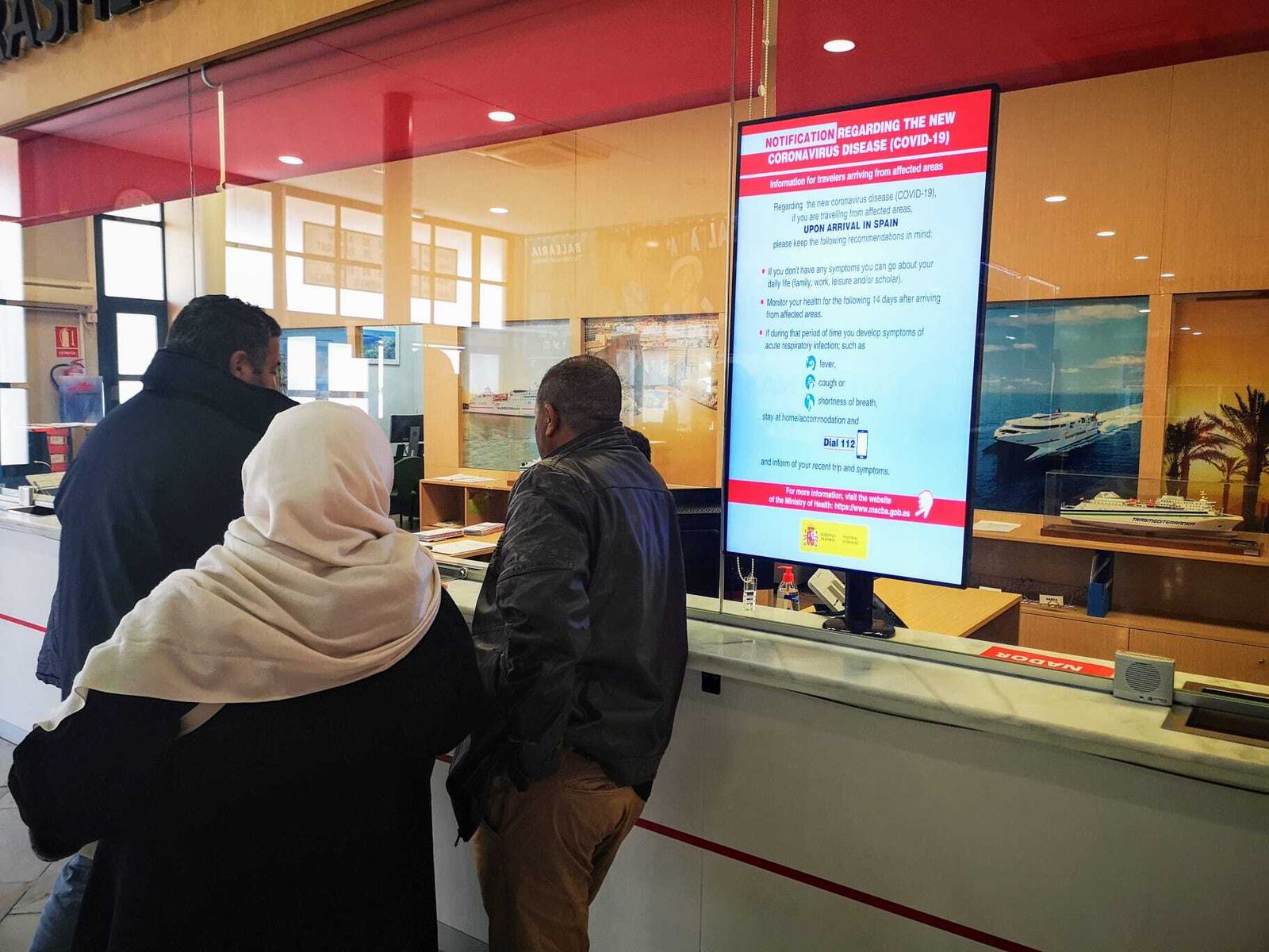 Varias personas en el punto y información y ventas del Puerto con las medidas por la Covid en el panel.