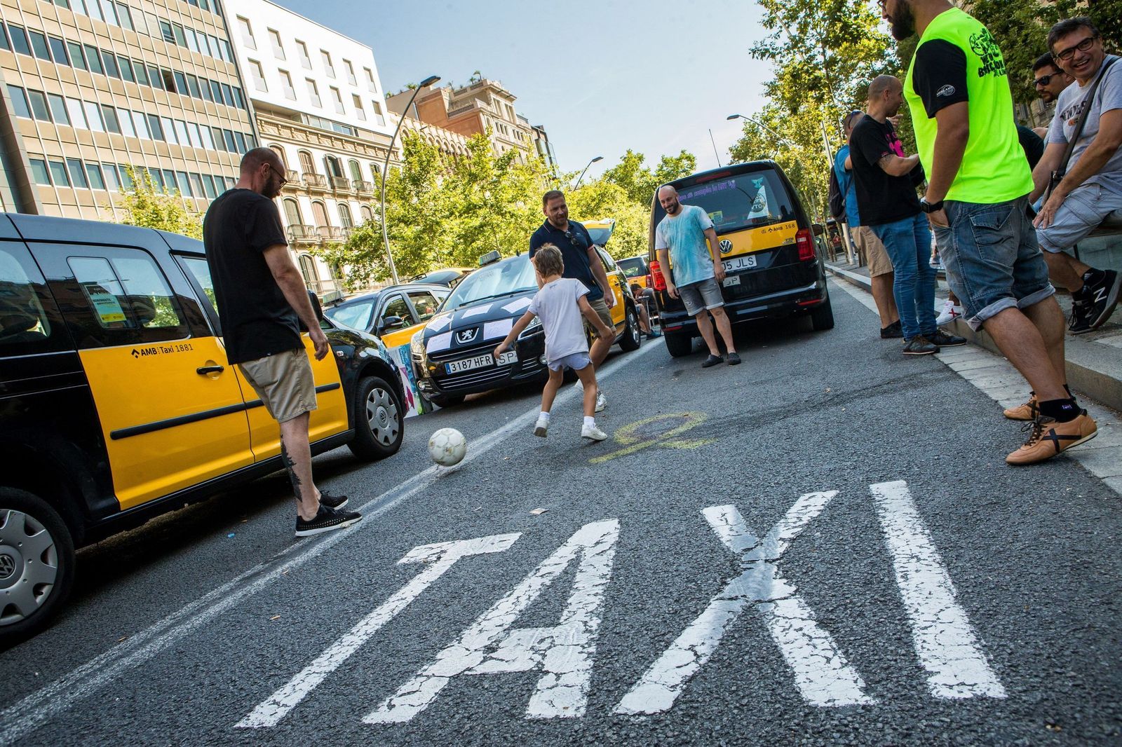 Varios taxistas juegan al fútbol con un niño en el centro de Barcelona.