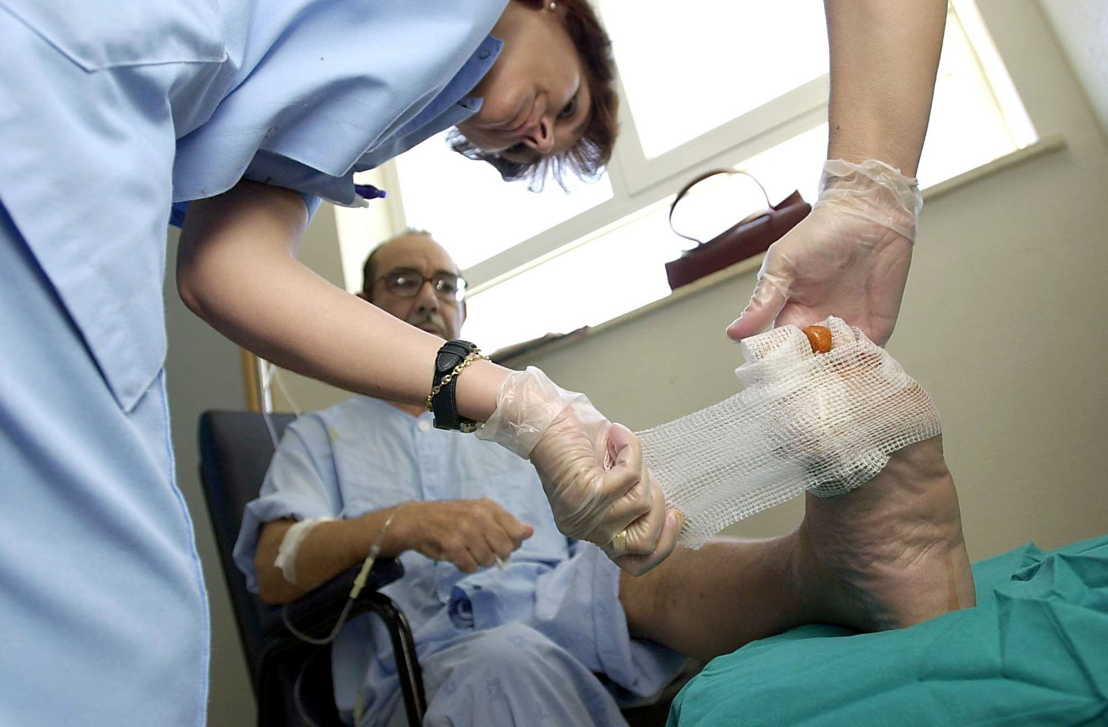 Dos enfermeras curan a un paciente operado del pie.