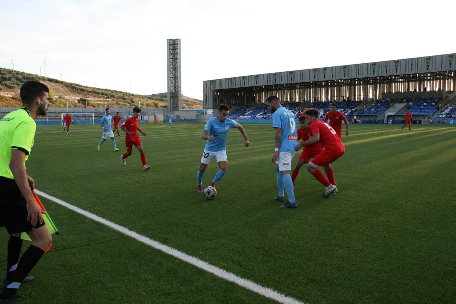 Mario Sánchez intenta esquivar la presión de dos rivales ante la mirada de Juan Delgado