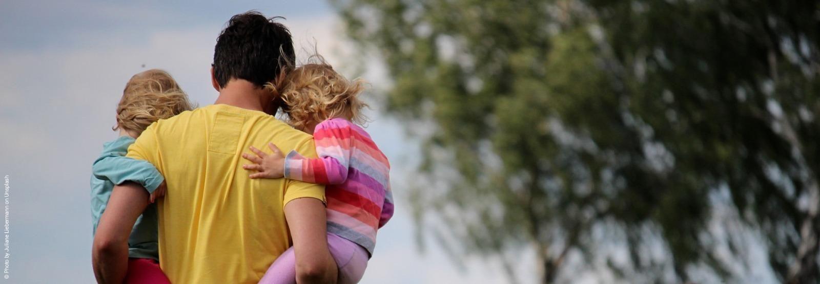 Un padre sostiene en brazos a sus dos hijas.